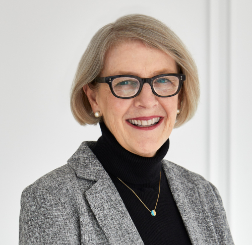 Photo of the author, Audrey Danaher, wearing glasses, a black turtleneck sweater, gold necklace and a grey jacket